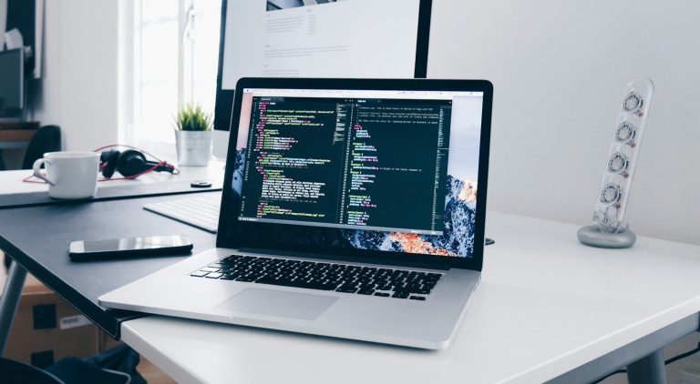A MacBook with lines of code on its screen on a busy desk